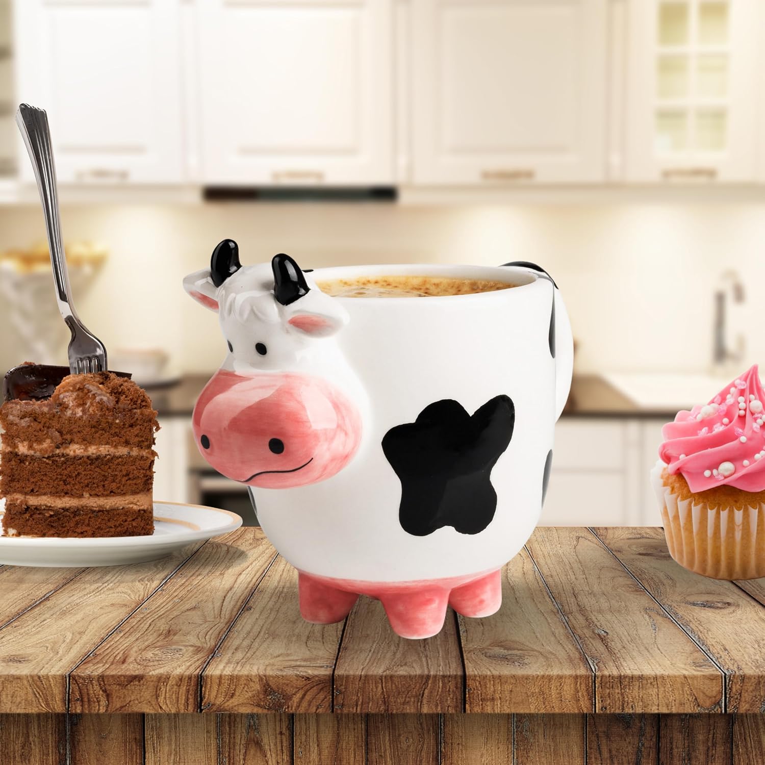 A SWEETLO cow-shaped coffee mug on a wooden kitchen table with cake and a pink cupcake.